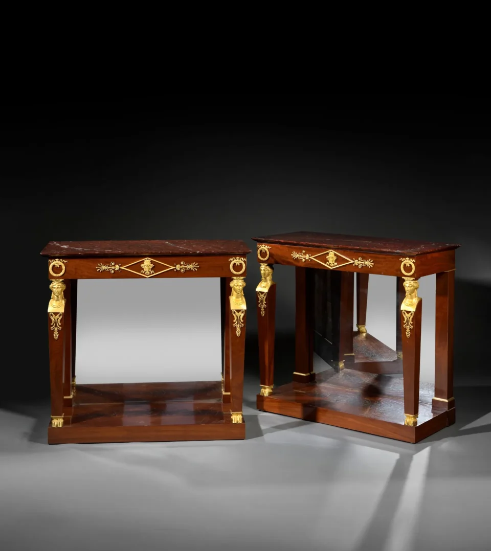 Paire de table consoles en acajou, le dessus de marbre griotte à moulure inversée reposant sur une ceinture à couronnes de feuilles de laurier et ruban et mascaron. Adjugé à 19 500 €