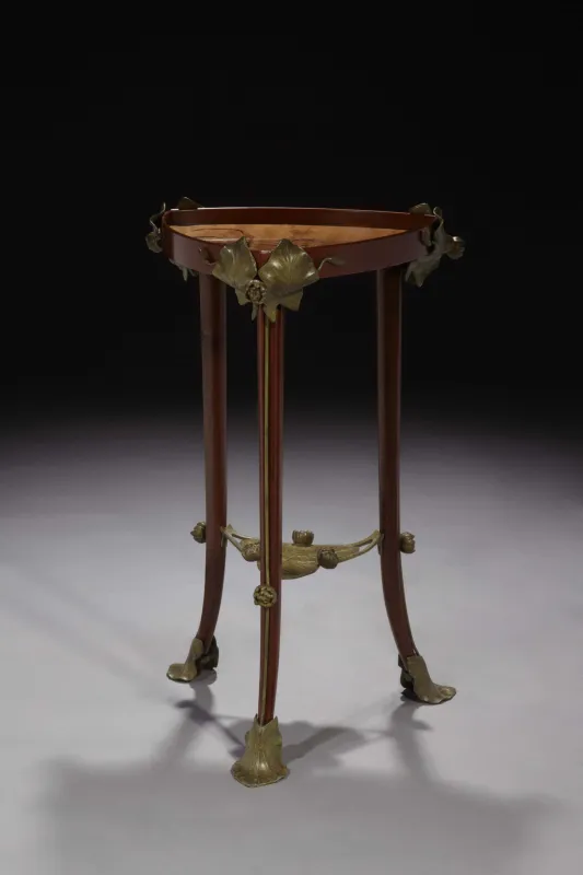Louis MAJORELLE (1859 - 1926) Précieux guéridon en acajou orné de nénuphars en bronze patiné vert. Plateau cuvette à décor de narcisses en marqueterie de bois divers.