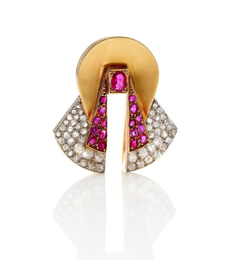 RAYMOND TEMPLIER - ANNÉES 1935 CLIP COCARDE RUBIS ET DIAMANTS Il porte un rubis plus important au centre sur un double pavage de rubis et diamants. Monture en or jaune 18K et platine.Adjugé à 3 000 €